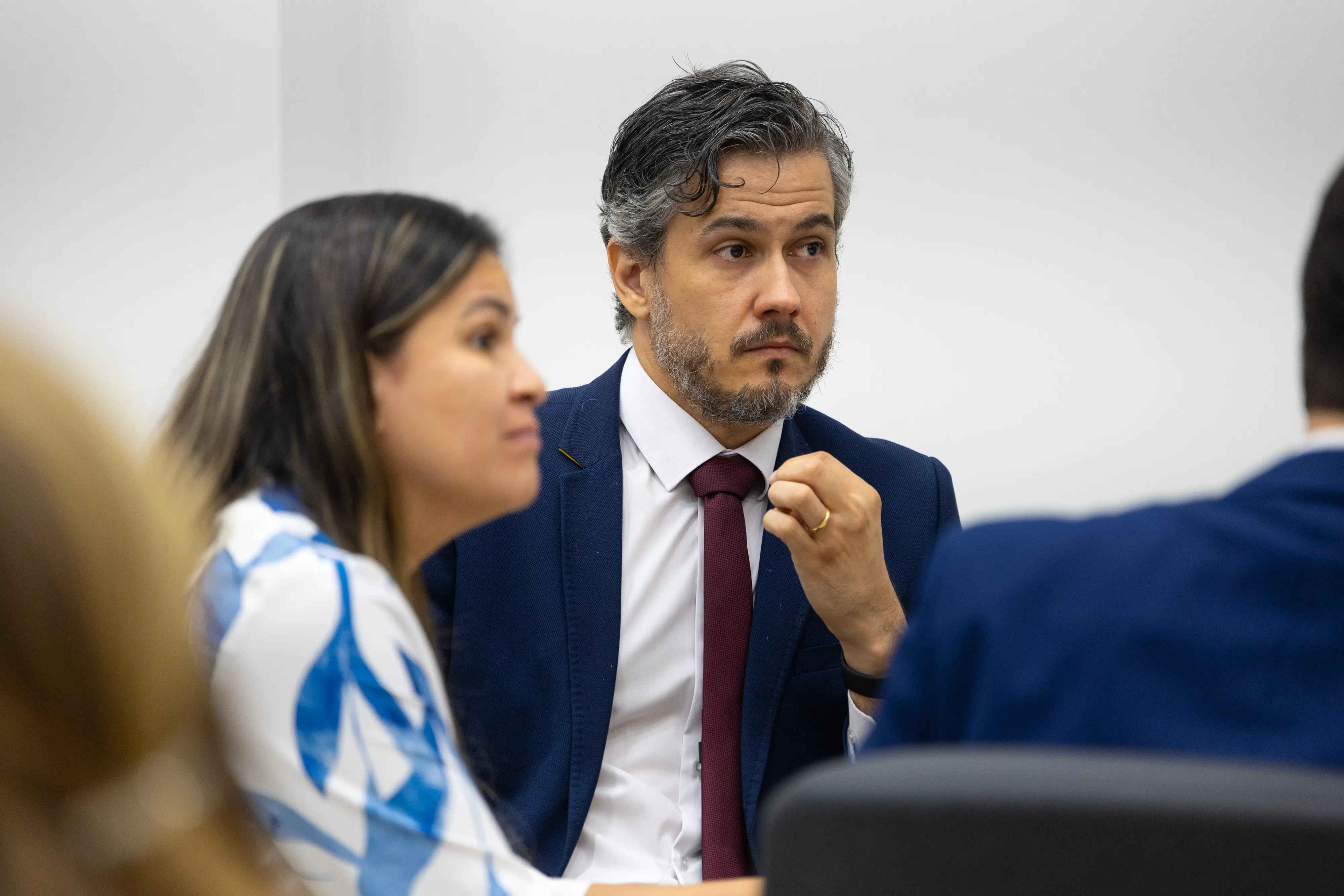 Homem de terno e gravata vermelha conversa com participante durante dinâmica em grupo.