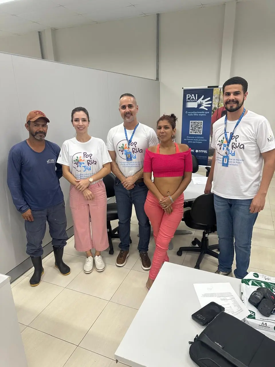 Cinco pessoas posam em pé dentro de um escritório. Três vestem camisetas brancas do projeto 