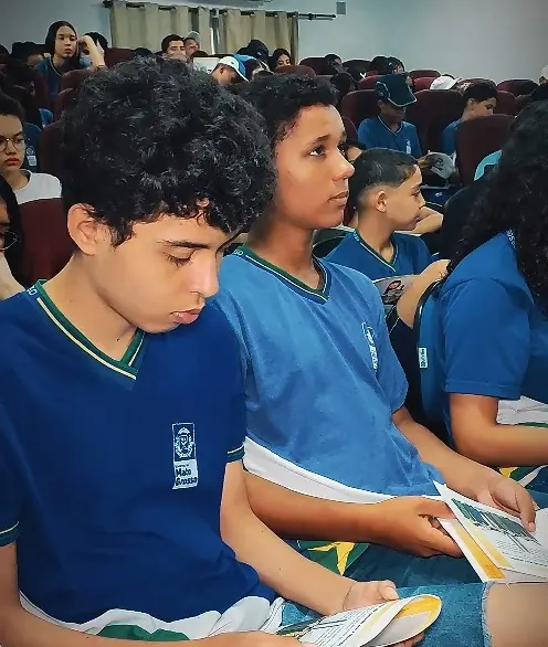 Vários estudantes sentados usando uniforme azul lendo a cartilha do Nosso Judiciário