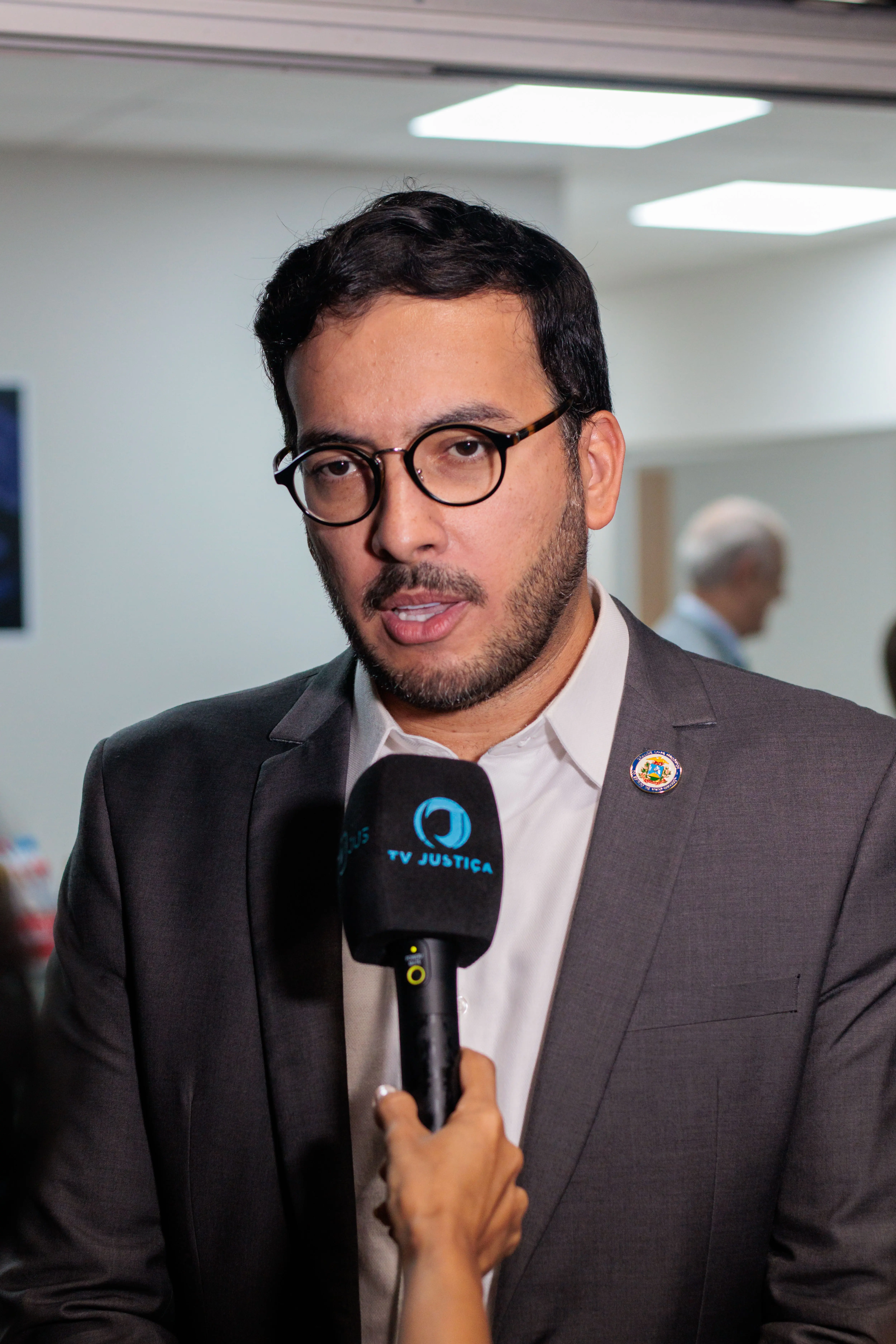Pedro Calazans, da Maçonaria, que contribui com doações apra casa de amparo, concede entrevista. Ele é um homem branco, com barba cerrada, usa óculos com armação escura, blaser cinza e camisa branca