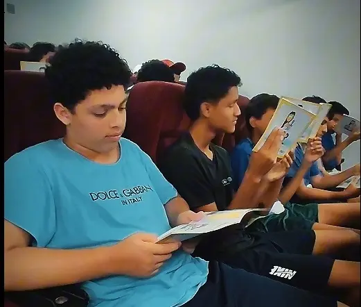 Foto em ângulo fechado de jovens sentados, lendo a cartilha do Nosso Judiciário
