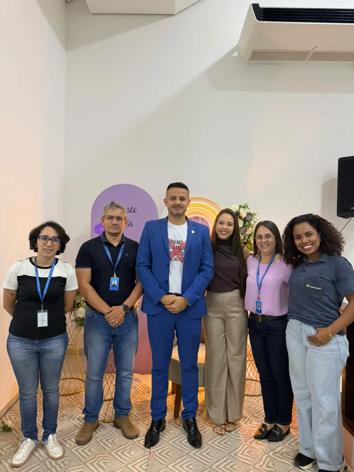 Foto vertical que mostra o juiz Anderson Fernandes posando para a foto ao lado de outro homem e quatro mulheres, que usam crachá de servidores do Judiciário.