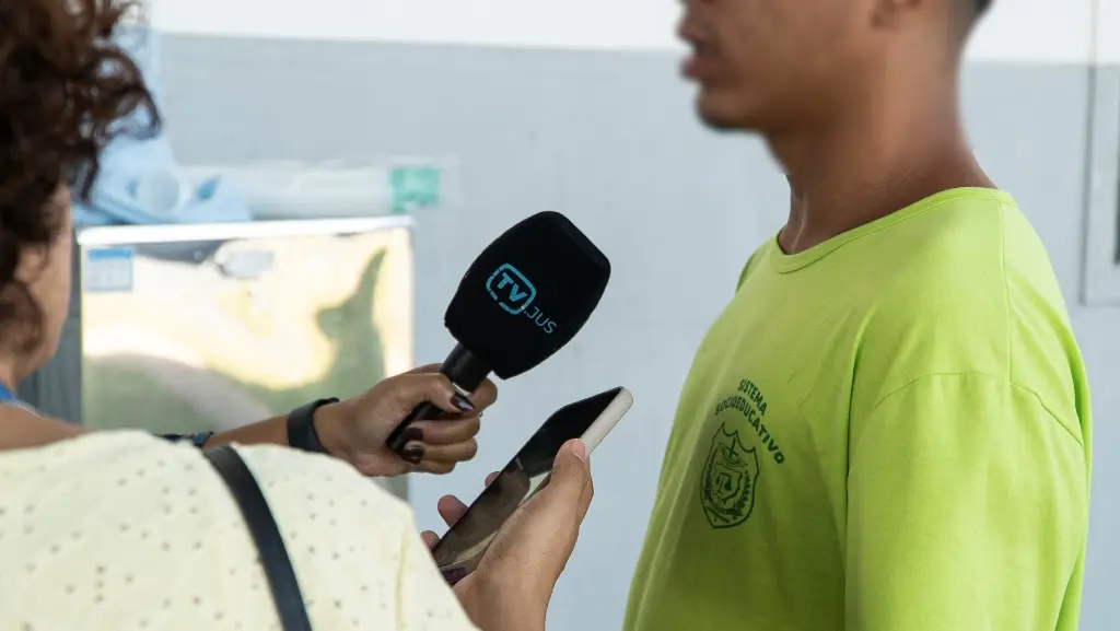 Foto horizontal que mostra um adolescente em medida socioeducativa concedendo entrevista à TV Justiça. Ele é negro e usa camiseta verde neon do centro socioeducativo.