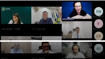 Mosaico de videoconferência com sete pessoas visíveis em dois blocos de linhas. Cada participante está em seu ambiente, alguns com fones de ouvido e microfones. Ícones circulares com iniciais identificam alguns usuários à direita.