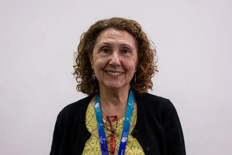 Foto que mostra Gisele Molinari, diretora da Subsecretaria de Comunicação, Conhecimento e Inovação e membro do JusLab da Justiça Federal de São Paulo do busto pra cima, sorrindo. Ela é uma senhora branca, de cabelo curto, cacheado e castanho claro, usando blusa verde estampada e cardigan preto.