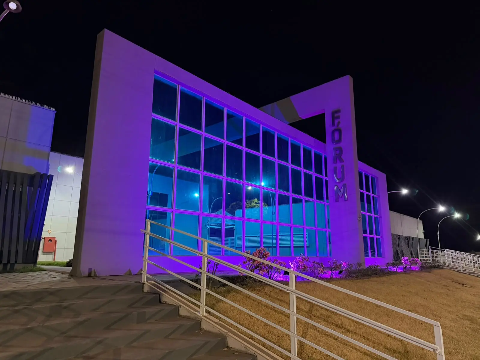 Foto horizontal que mostra a fachada do fórum de Mirassol D'Oeste com iluminação lilás em alusão à campanha Agosto Lilás.
