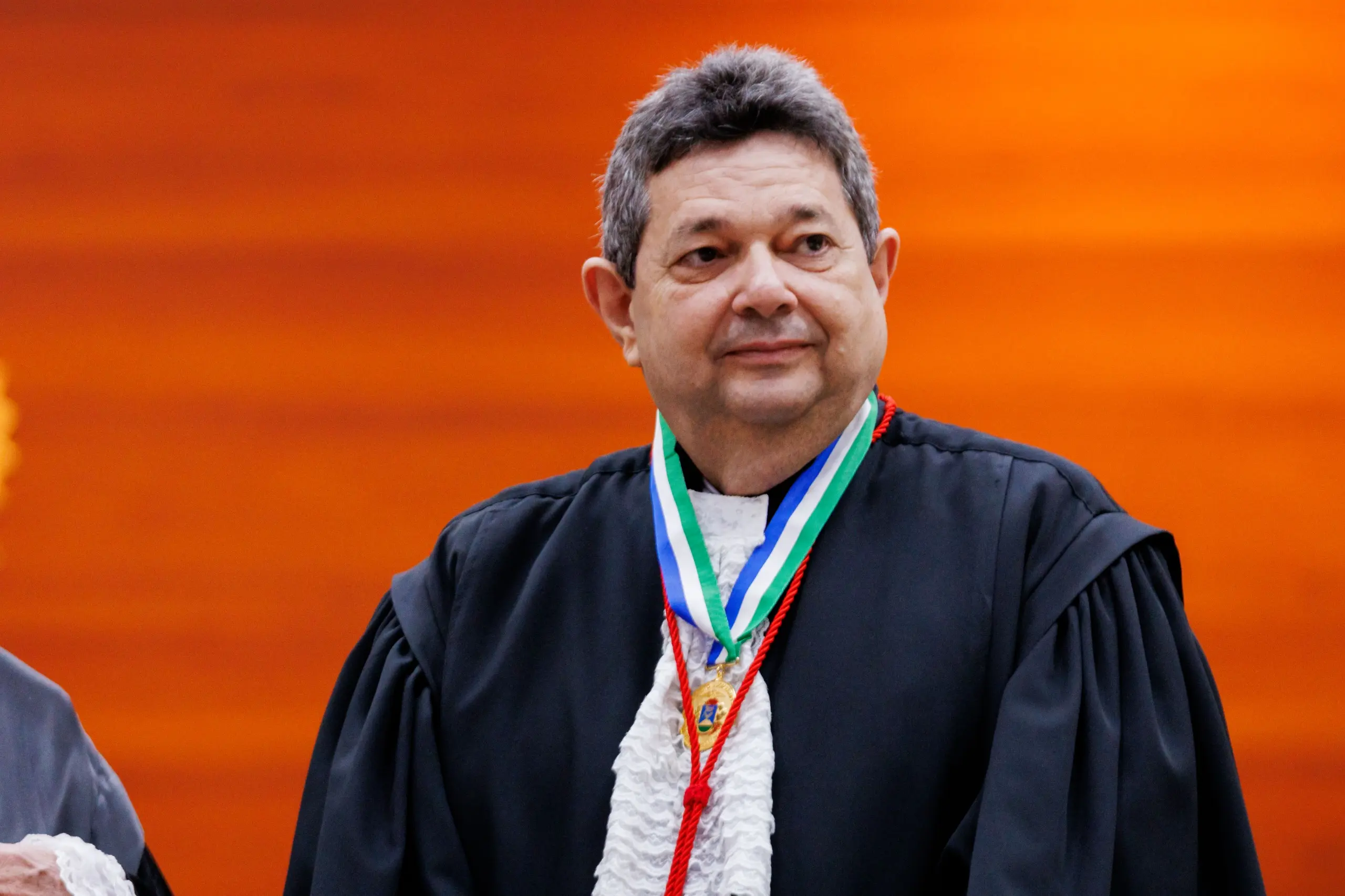 Foto horizontal colorida do corregedor José Lindote. Ele é um homem branco, de c abelos curtos grisalhos. Usa toga de gala preta com babados brancos na frente e medalha envolta do pescoço