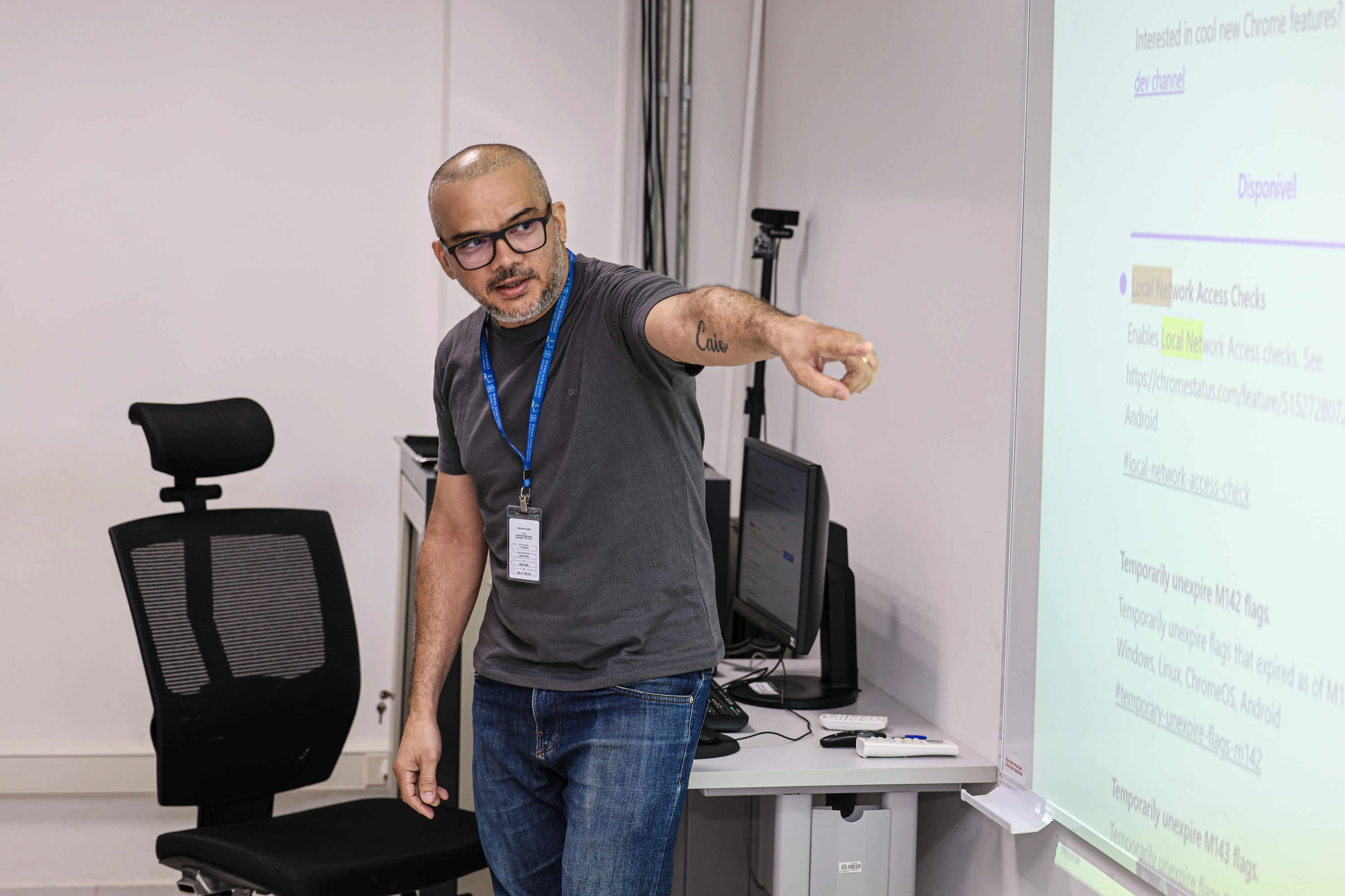 Instrutor aponta para a tela projetada e orienta participantes durante aula técnica em ambiente institucional.