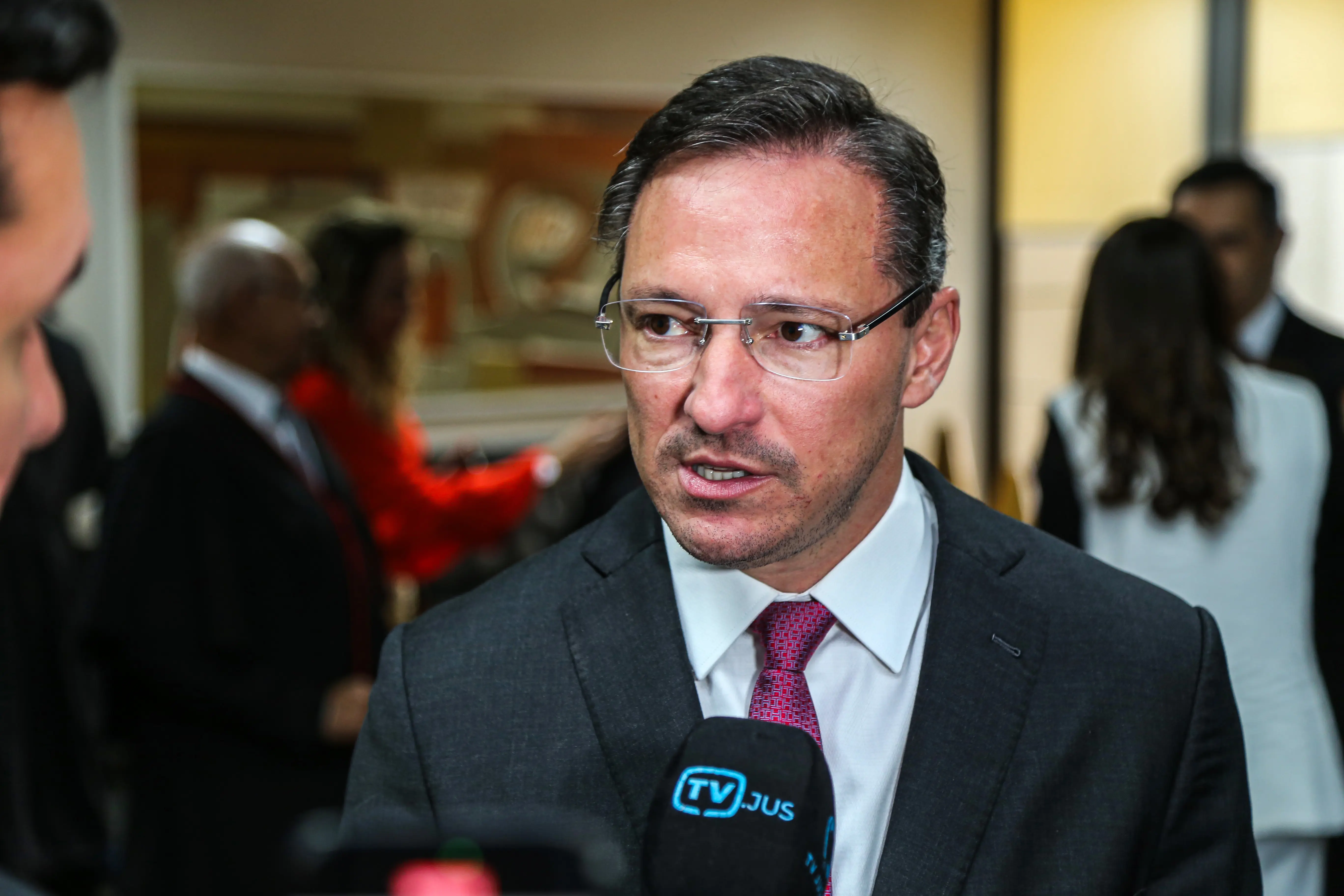 Homem de terno escuro concede entrevista à TV Justiça. Expressão concentrada durante declaração em ambiente interno do tribunal.