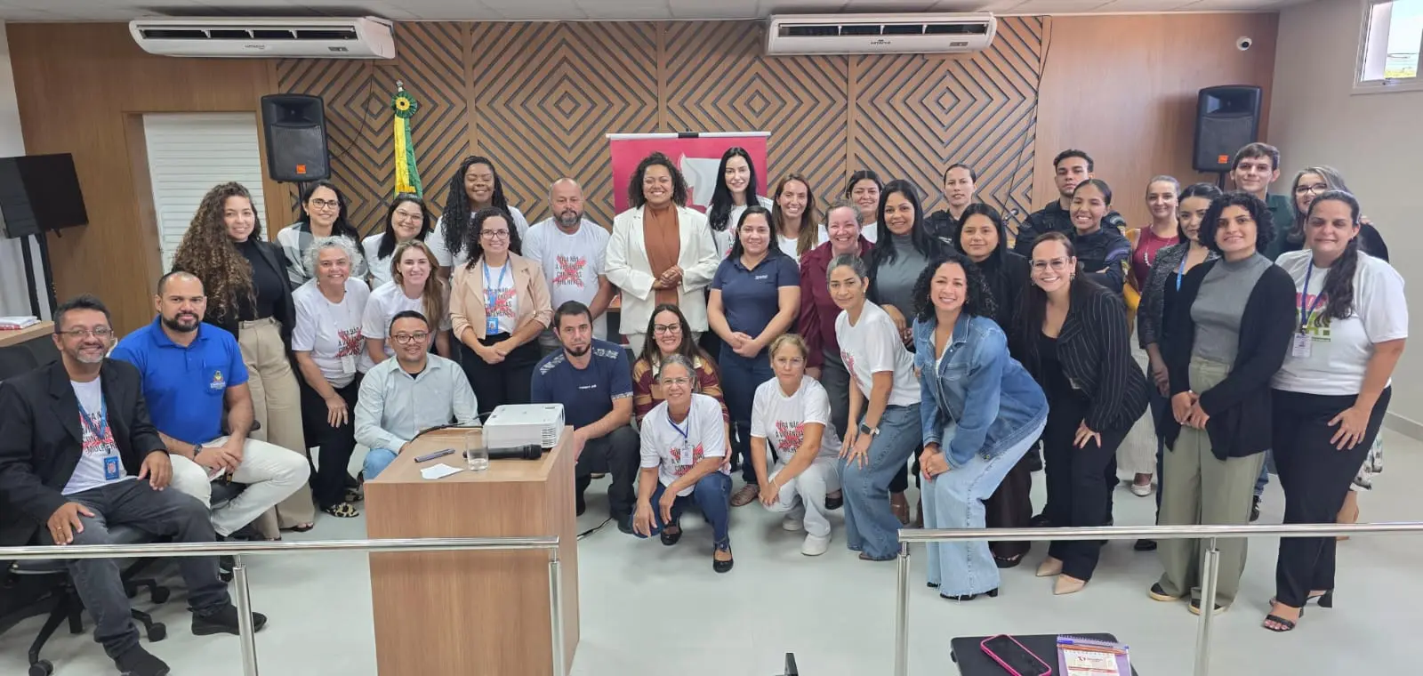 Foto horizontal colorida, em plano aberto, que mostra mais de 30 pessoas posando para a foto, no plenário do júri do Fórum de Tapurah. Tratam-se de membros da rede de enfrentamento à violência contra a mulher.
