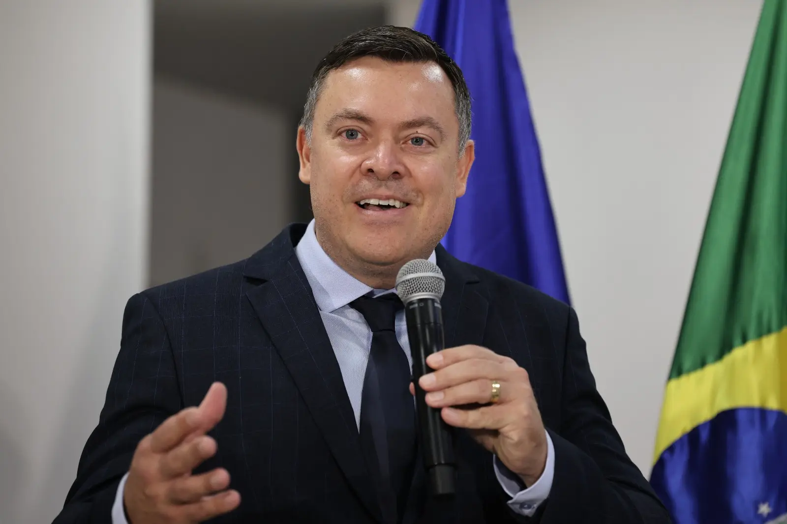 uiz diretor do Foro da Comarca de Chapada dos Guimarães, Leonísio Salles de Abreu Júnior, aparece segurando um microfone e falando aos participantes, ao fundo a bandeira do Brasil.