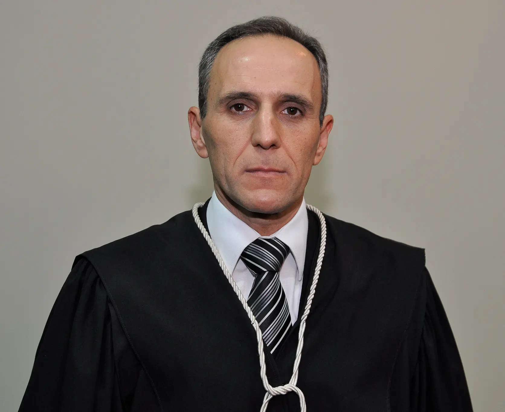 Juiz Alcindo Peres da Rosa, titular da Comarca de Juscimeira. ele é um hoem branco, de olhos castanhos, cabelos grisalhos, usando camisa branca, gravata e toga.