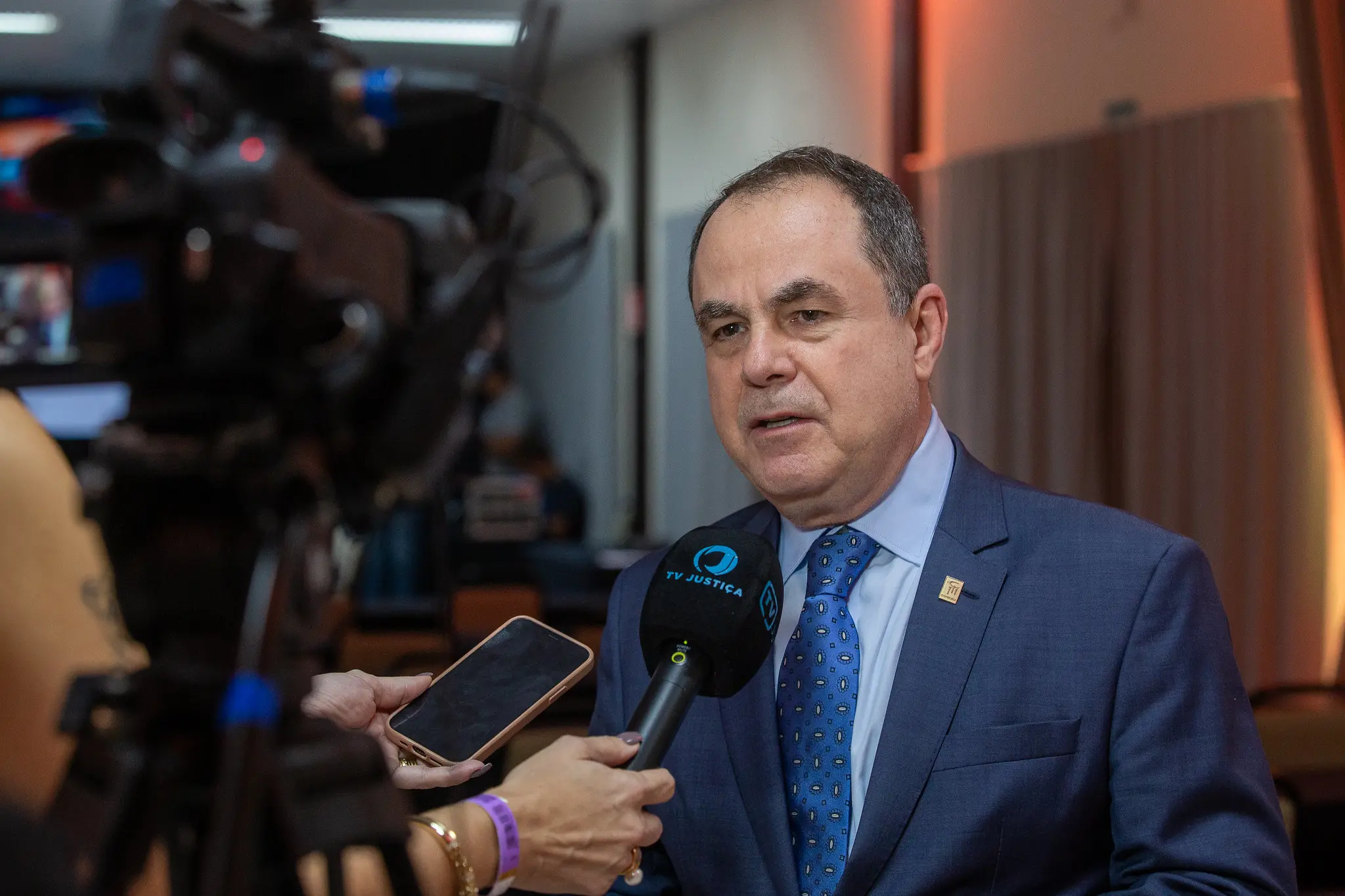 Foto que mostra o presidente do Copedem, desembargador Marco Villas Boas, concedendo entrevista à TV Justiça. Ele é um homem branco, de olhos castanhos e cabelos levemente grisalhos, usando camisa azul clara, terno azul marinho e gravata azul com estampa amarela.  