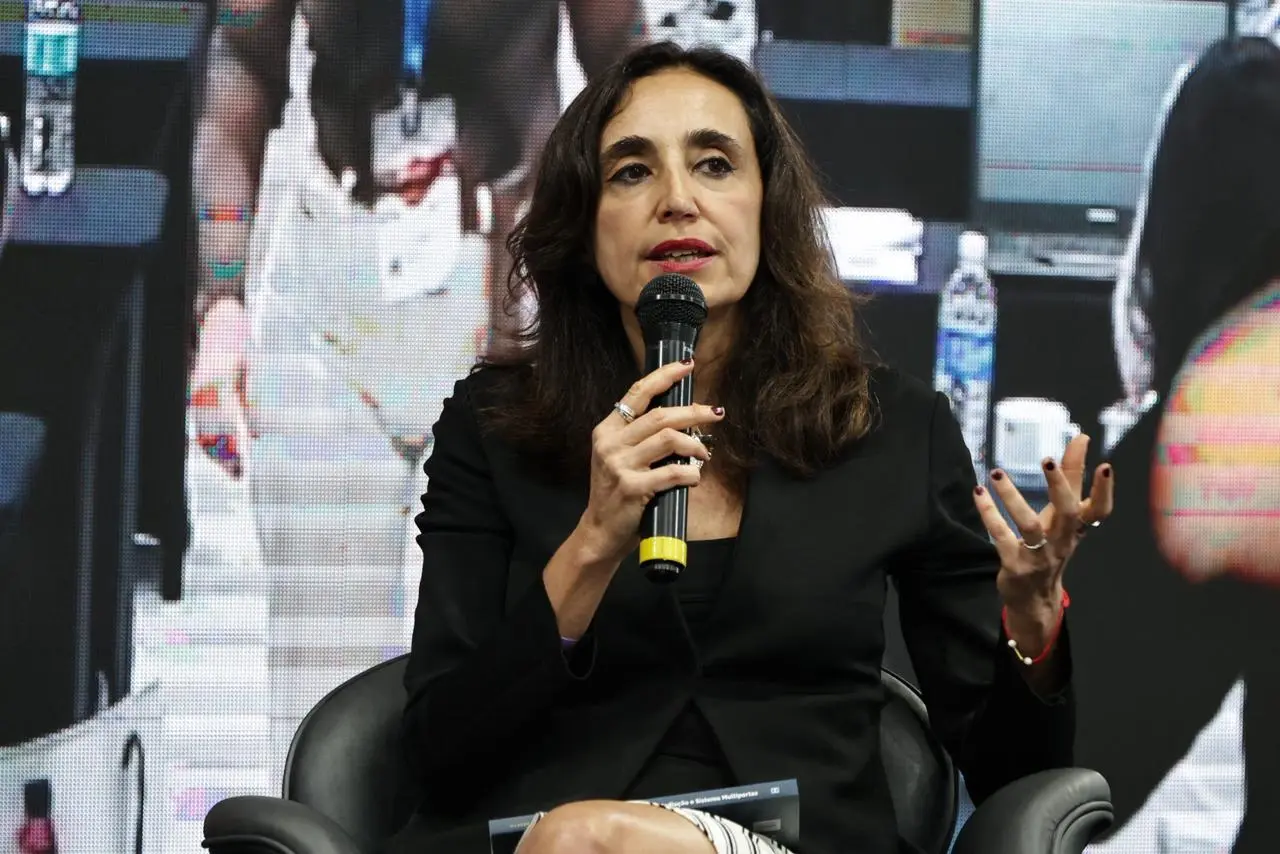 Juíza Valéria Lagrasta sentada em uma poltrona e falando ao microfone. Ela é uma mulher branca, magra, de cabelos lisos e castanhos, olhos castanhos, usando blusa e blazer pretos.