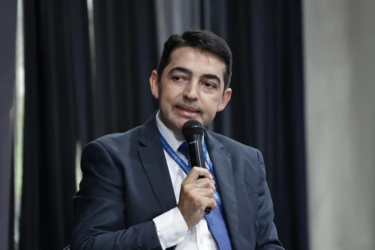 Primeiro vice-presidente do Fonamec, juiz Juliano Carneiro Veiga, fala ao microfone. Ele é um homem branco, de cabelos e olhos escuros, usando camisa branca, gravata azul e terno cinza.