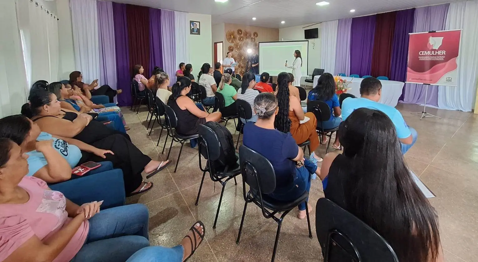 Foto horizontal em plano aberto que mostra um salão repleto de pessoas sentadas, assistindo à palestra da juíza Tatyana Lopes, que está à frente, em pé, com o microfone na mão. 
