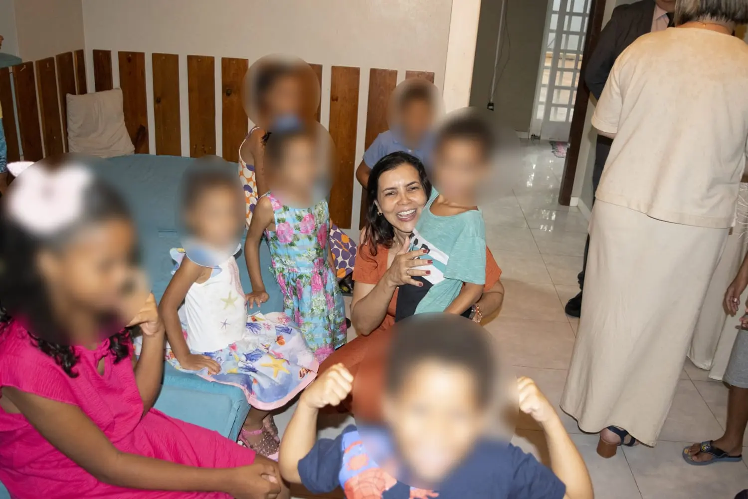 A juíza auxiliar da Corregedoria está abaixada, abraçando uma criança. Ao redor dela estão as demais crianças da casa-lar.