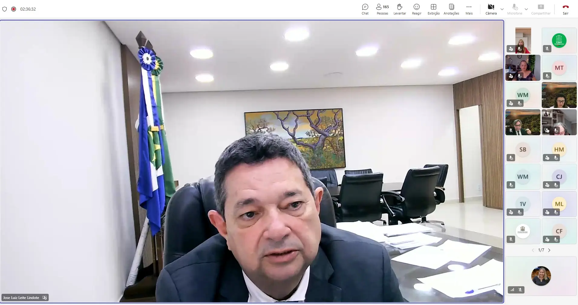 Captura de tela de reunião virtual. O corregedor-geral da Justiça de Mato Grosso, desembargador José Luiz Leite Lindote, aparece em primeiro plano, sentado em mesa de trabalho, falando durante o seminário. Ao fundo há uma sala de reuniões com cadeiras, mesa, bandeiras e um quadro na parede