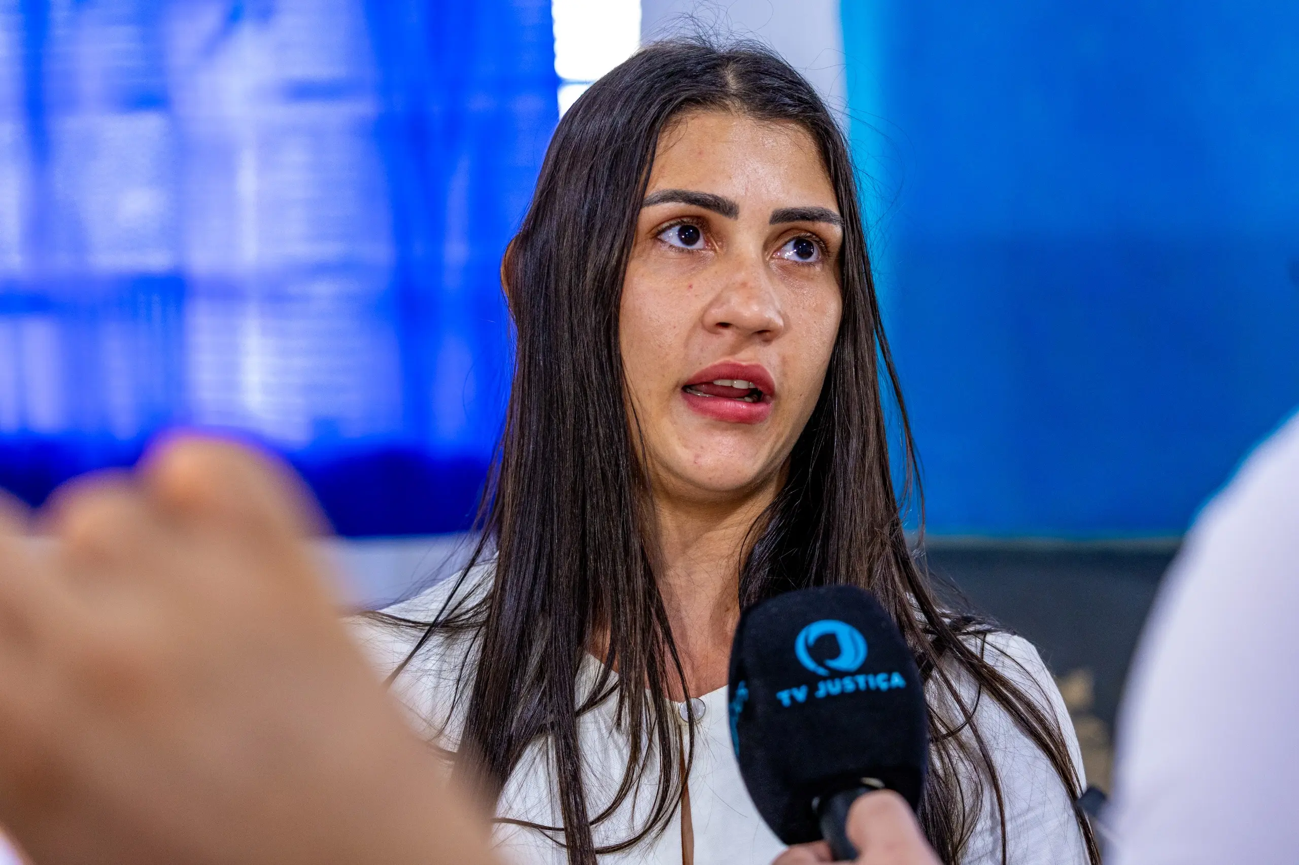 Mulher jovem, de cabelos longos e expressão séria, concede entrevista à TV Justiça. Diante do microfone, ela relata sua experiência no atendimento recebido durante ação social realizada pelo projeto.