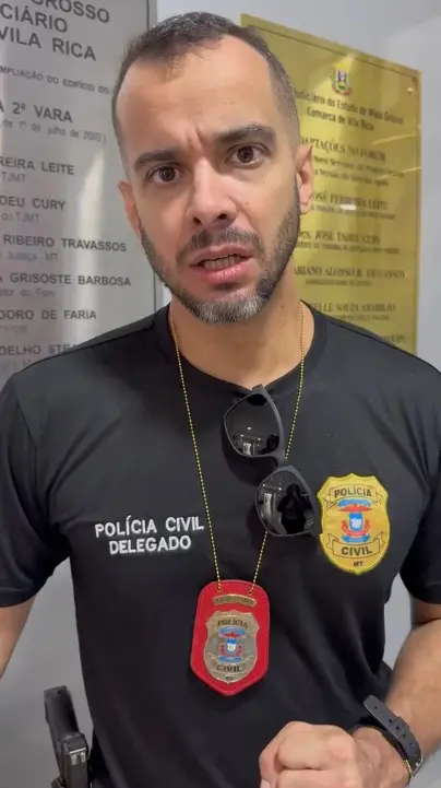 Foto vertical que mostra o delegado Luís Roberto Freitas, da cintura pra cima, olhando para a câmera. Ele é um homem branco, de olhos e cabelos castanhos, barba grisalha. Ele usa camiseta e distintivo da Polícia Civil e tem uma arma na cintura.