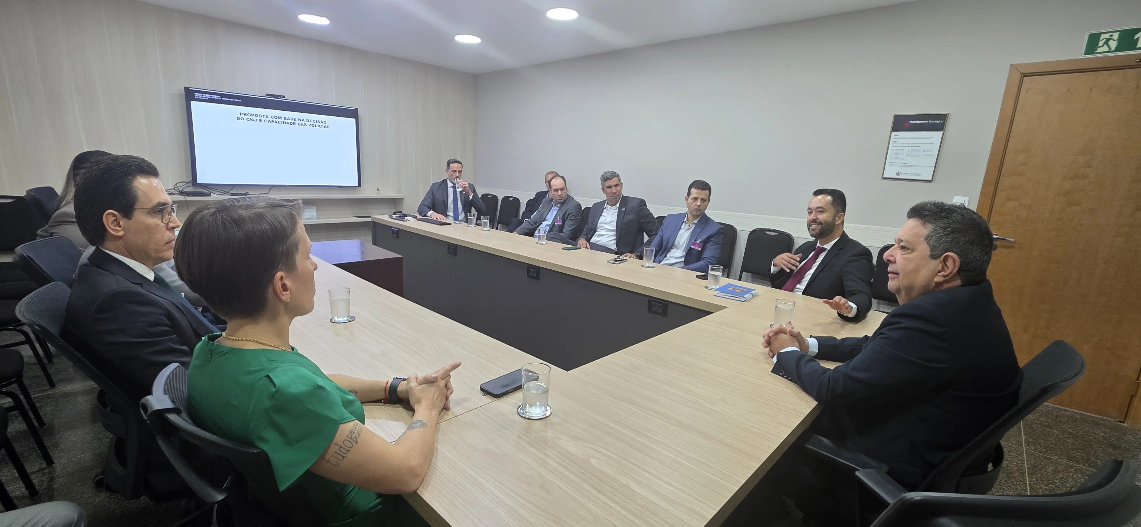 Representantes da Corregedoria e da Secretaria de Estado de Segurança Pública estão sentados ao redor de uma mesa em formato de "U". Ao centro está o corregedor-geral da Justiça; desembargador José Luiz Leite Lindote, à direita dele, o juiz auxiliar da Corregedoria, João Filho de Almeida Portela; e,