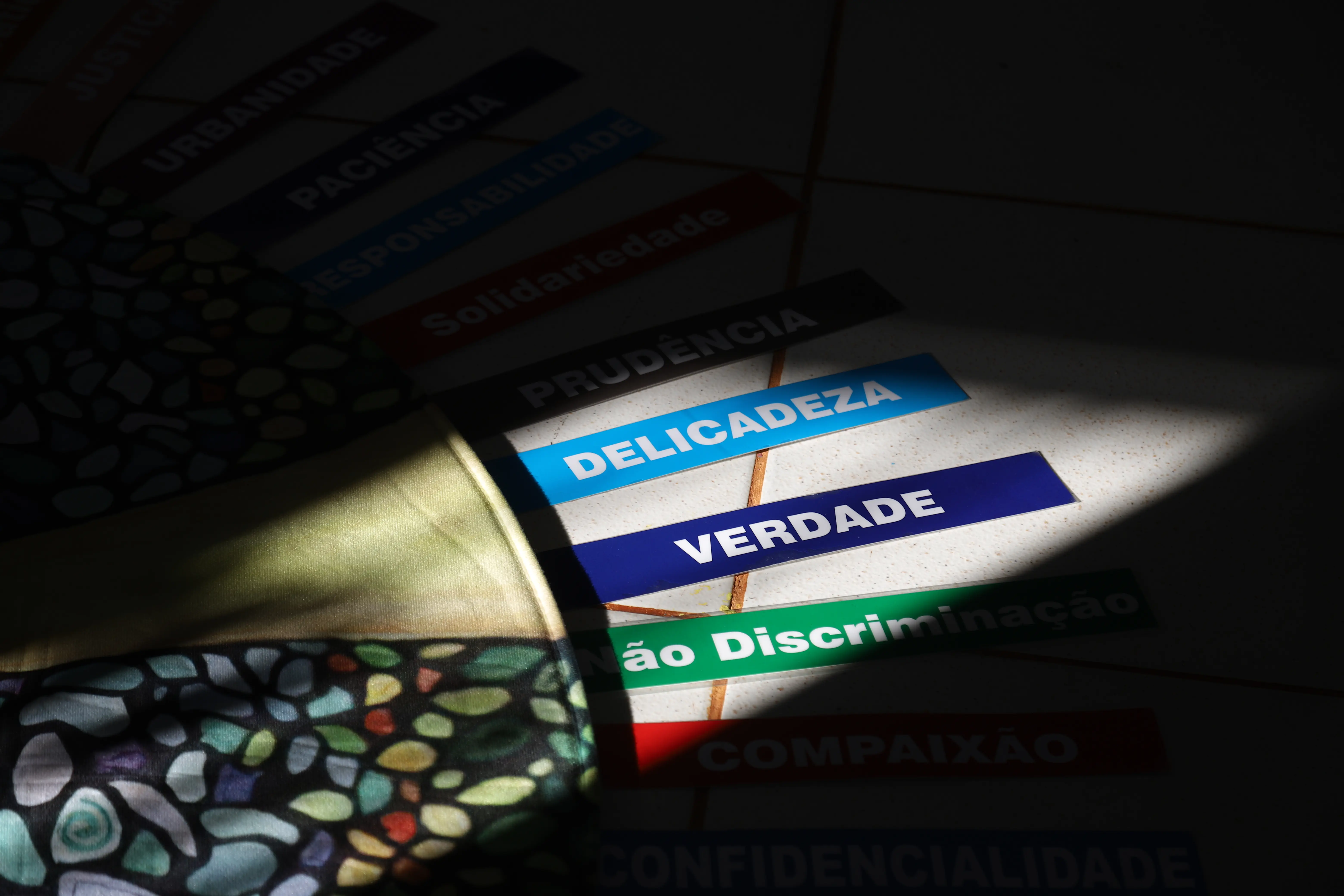 Feixe de luz ilumina parcialmente palavras como “Delicadeza”, “Verdade” e “Não Discriminação” dispostas ao redor de mandala em formato de árvore. A cena destaca o simbolismo e a reflexão promovida no círculo.