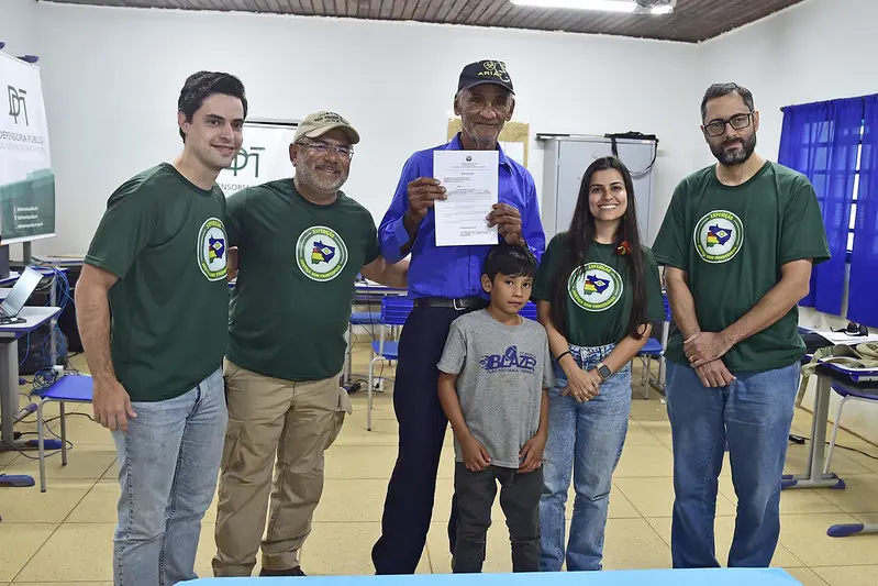 Foto que mostra o promotor de justiça, o juiz, o defensor público, uma servidora da Defensoria Pública, um idoso e um menino posando para a foto e sorrindo. O idoso segura um documento nas mãos: é a guarda provisória do neto, que obteve da Justiça.