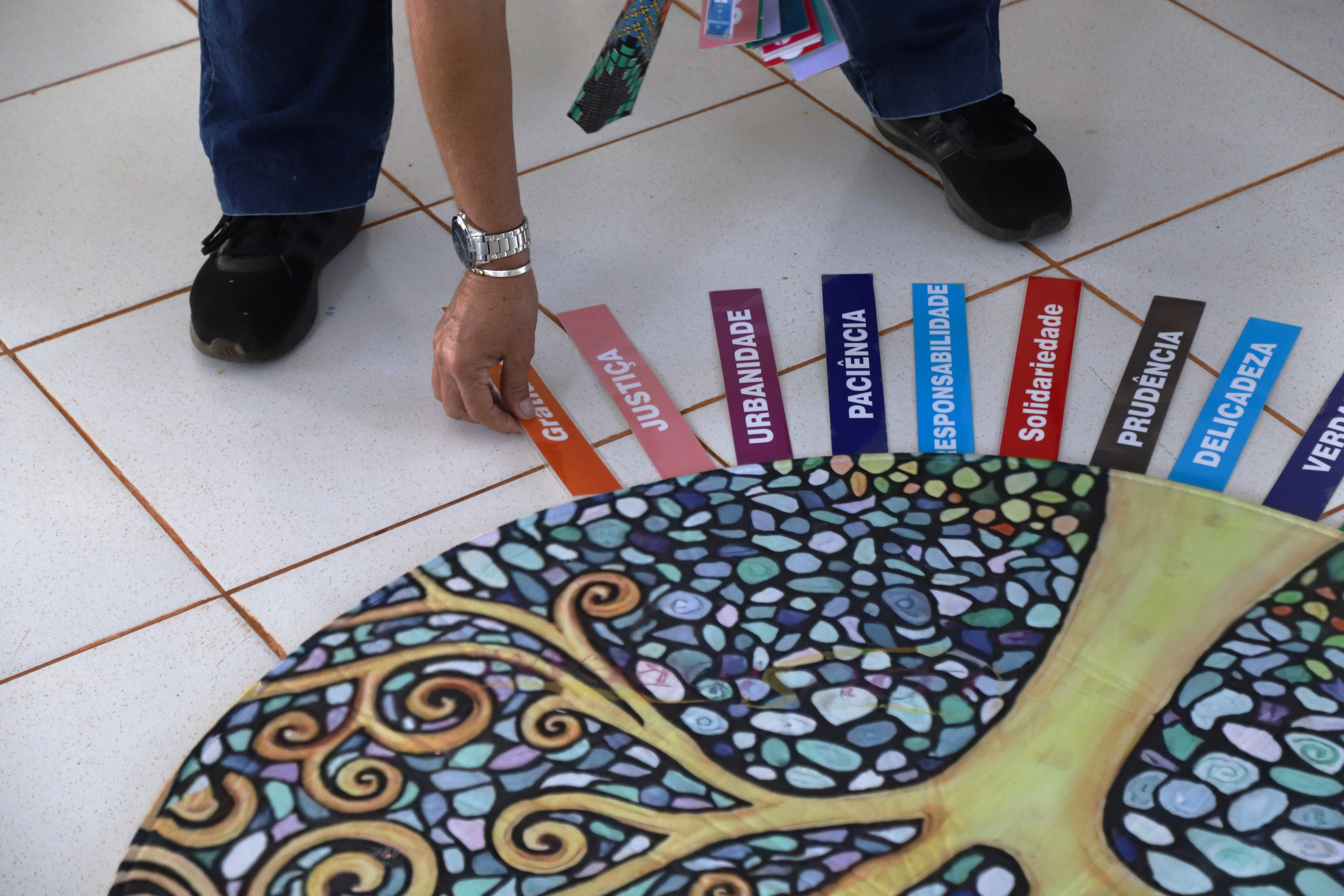Participante escolhe a palavra “Gratidão” entre várias qualidades dispostas ao redor de uma mandala. Termos como “Justiça”, “Solidariedade” e “Responsabilidade” completam o círculo de valores da atividade