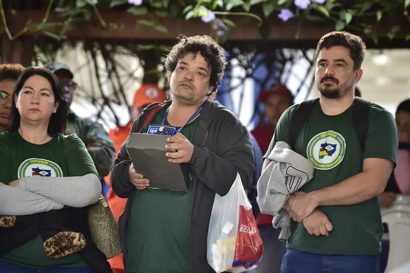 Equipe da Caixa Econômica Federal no pátio de uma escola. A mulher e dois homens usam camiseta verde da Justiça Sem Fronteiras.