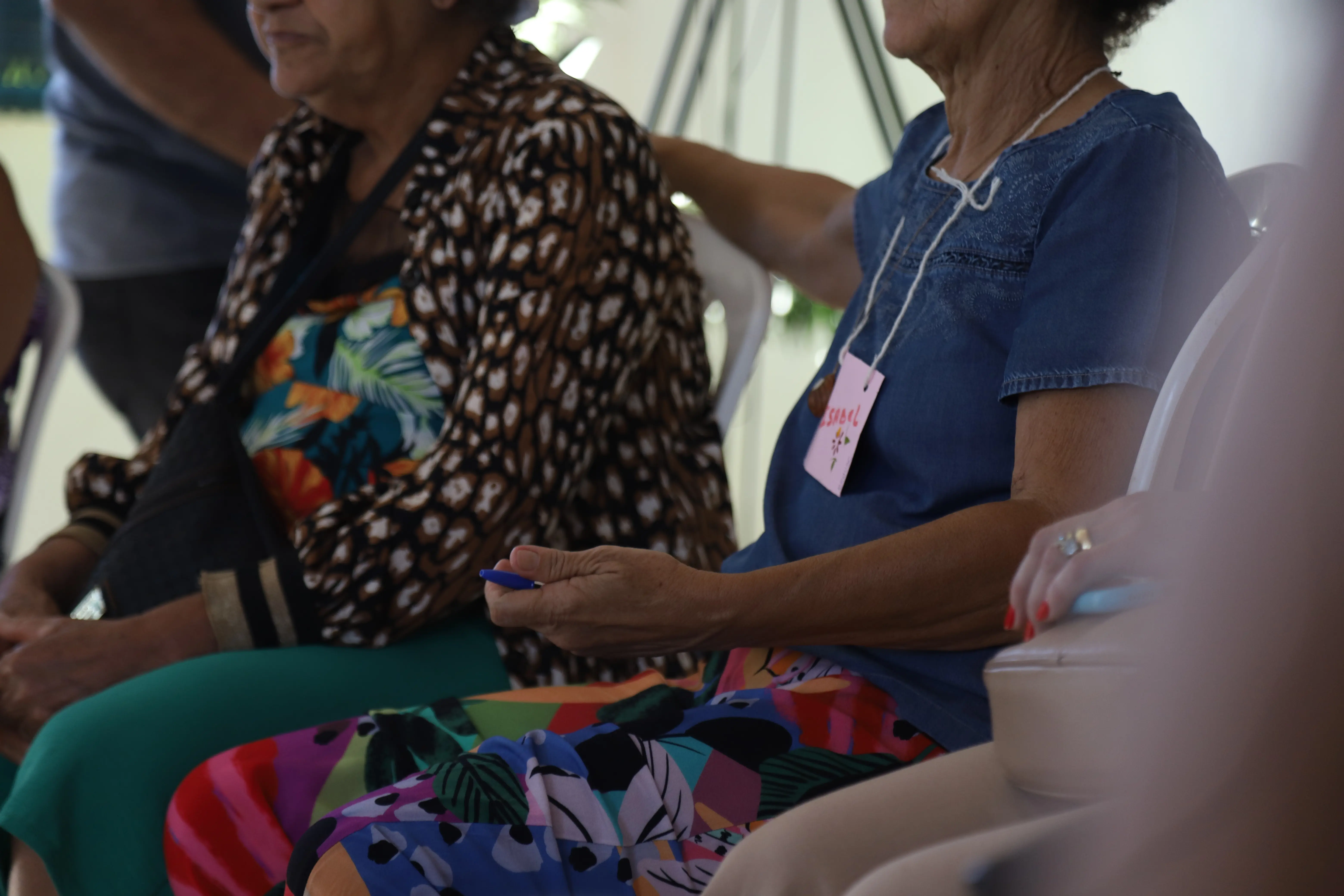Idosas sentadas em círculo participam de roda de conversa. Em destaque, mulher com crachá "ISABEL" segura um objeto simbólico, evidenciando envolvimento na dinâmica do Círculo de Construção de Paz.