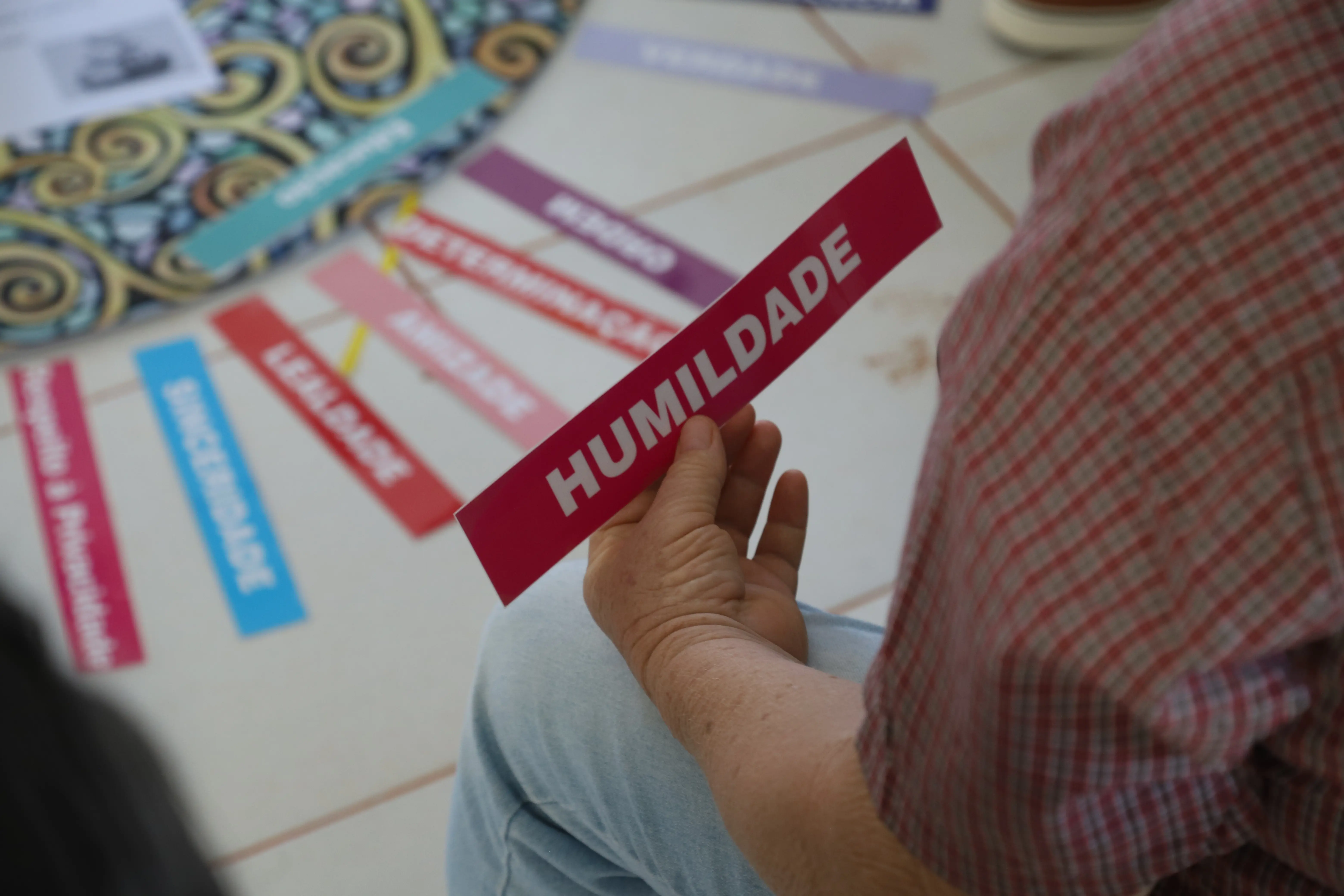 Pessoa segura a palavra “HUMILDADE” durante dinâmica no Círculo de Paz. Ao redor, outras palavras como “Sinceridade” e “Respeito” reforçam os princípios trabalhados no encontro