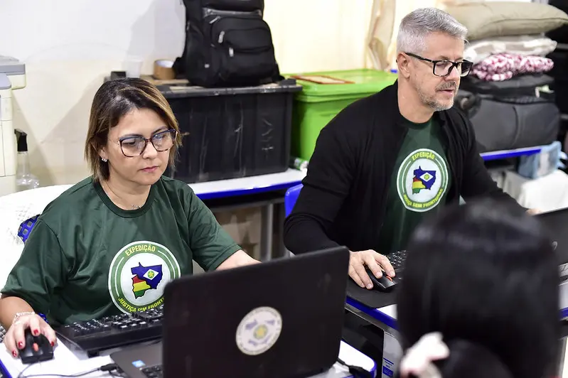 Servidora da Assembleia Legislativa e servidor da Politec realizam atendimento. Eles usam camiseta verde da Justiça Sem Fronteiras.