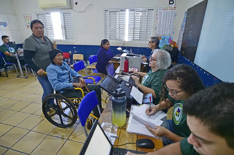 Servidores da Receita Federal e da Polícia Federal realizam atendimentos aos cidadãos, em uma sala de aula. Eles usam a camiseta verde musgo da Justiça Sem Fronteiras.