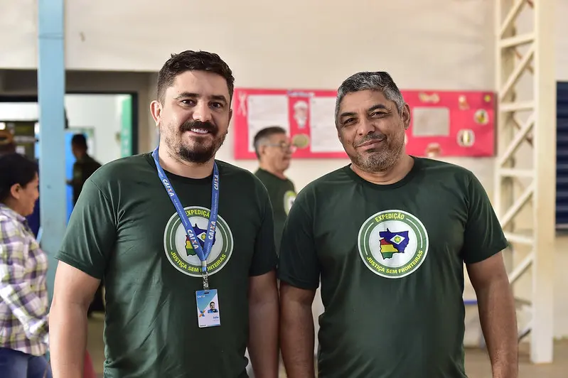Dois servidores da Caixa Econômica Federal posam sorrindo para a foto. eles usam camiseta verde da Justiça Sem Fronteiras.