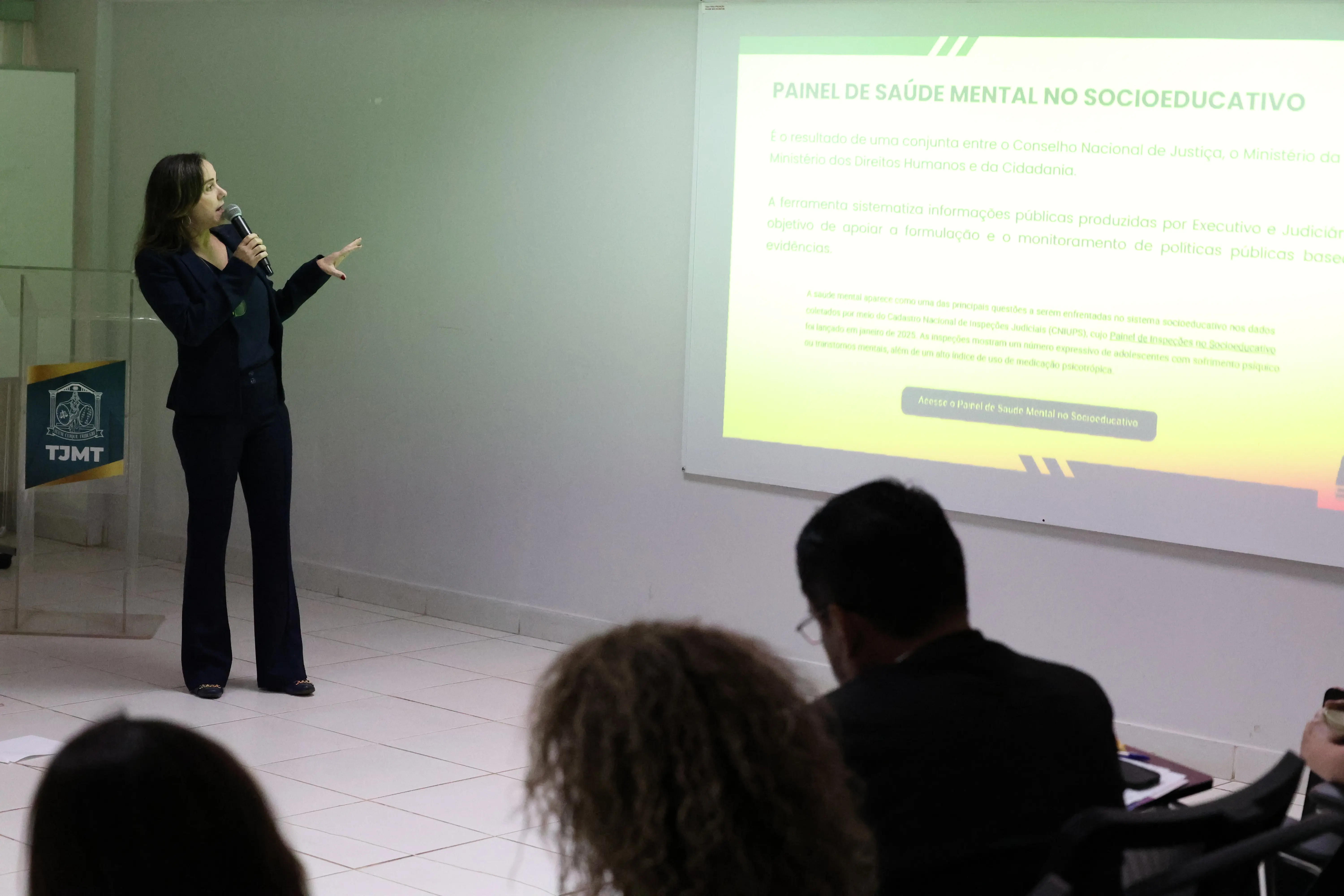 Juíza Leilamar usa terno azul apresenta painel sobre saúde mental no socioeducativo, apontando para a projeção