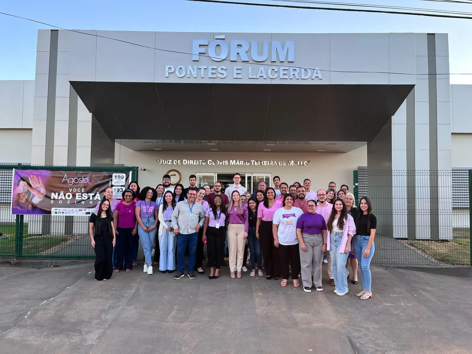 Diversas pessoas reunidas em frente ao Fórum de Pontes e Lacerda usando roupa lilás em alusão à campanha de combate à violência contra a mulher.
