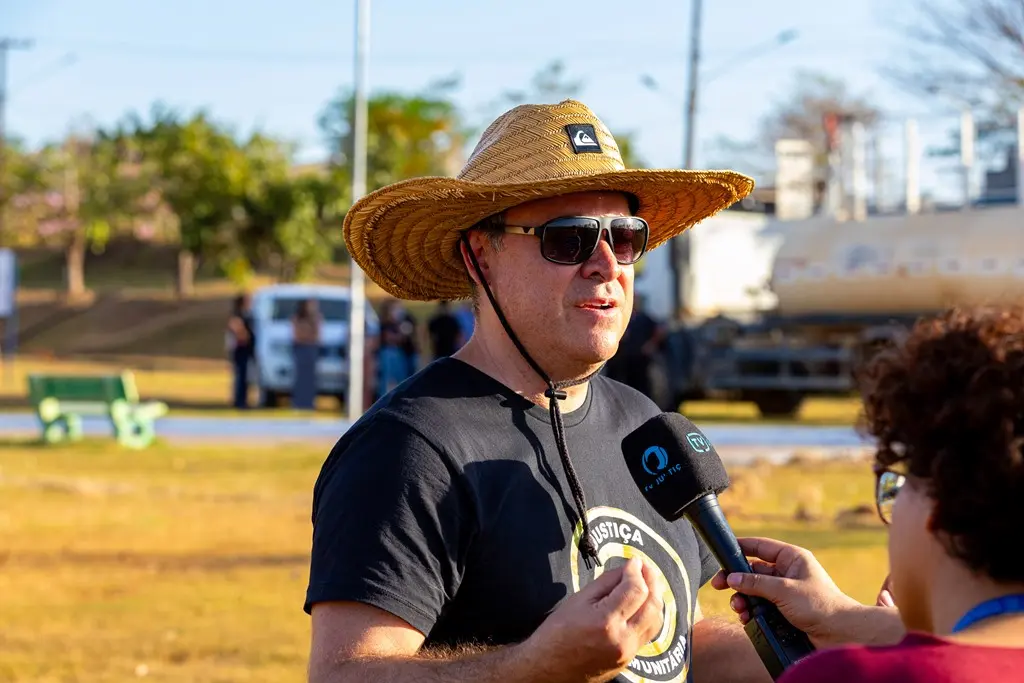 Juiz Leonísio Salles concede entrevista no parque ecológico de Nova Brasilândia. Ele é um homem branco, usando camiseta preta com a logo da Justiça Comunitária, óculos de sol e chapéu de palha.