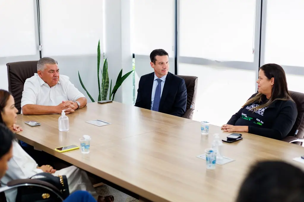 Desembargador Rodrigo Curvo, prefeito de Barra do Garças, Adilson Gonçalves, e supervisora de ESG da RZK Agro, Claudieli Peres, conversam em uma mesa de reunião.