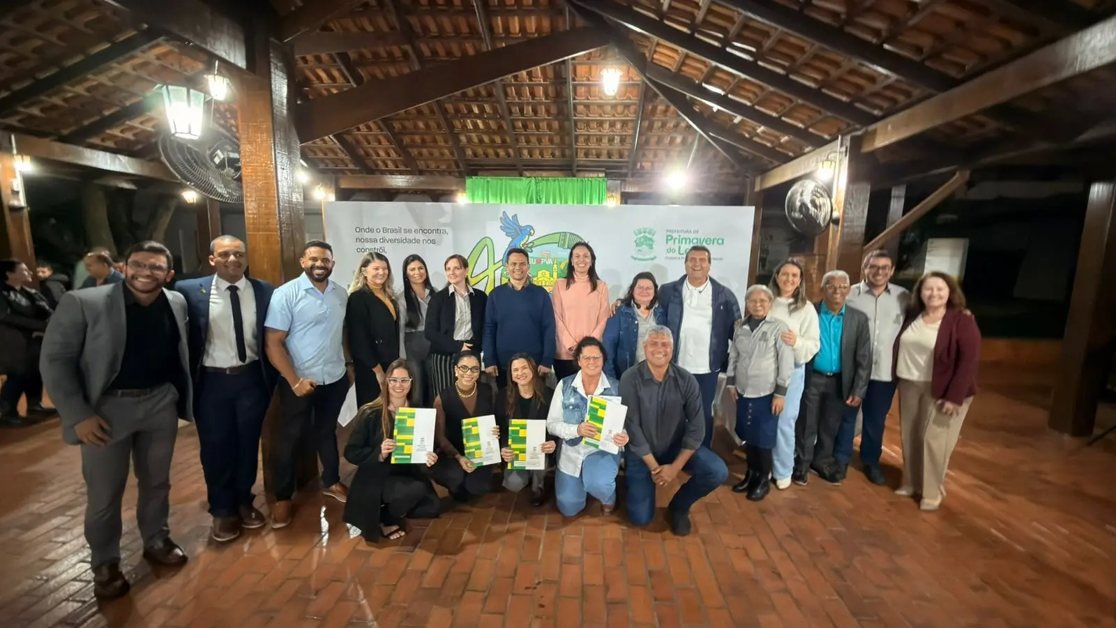 Autoridades, servidores municipais e moradores beneficiados posam para foto durante cerimônia de entrega de títulos definitivos de regularização fundiária em Primavera do Leste.