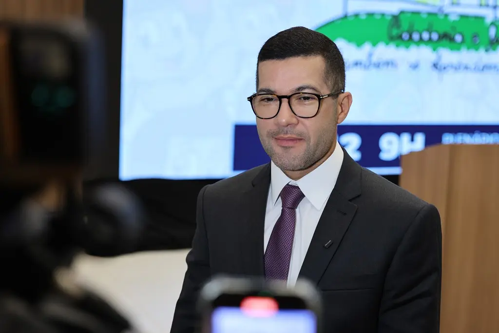 Juiz Ramon Fagundes Botelho durante entrevista. Ele é um homem branco, de cabelos e olhos castanhos, usando camisa branca, gravata roxa, terno preto e óculos de grau.