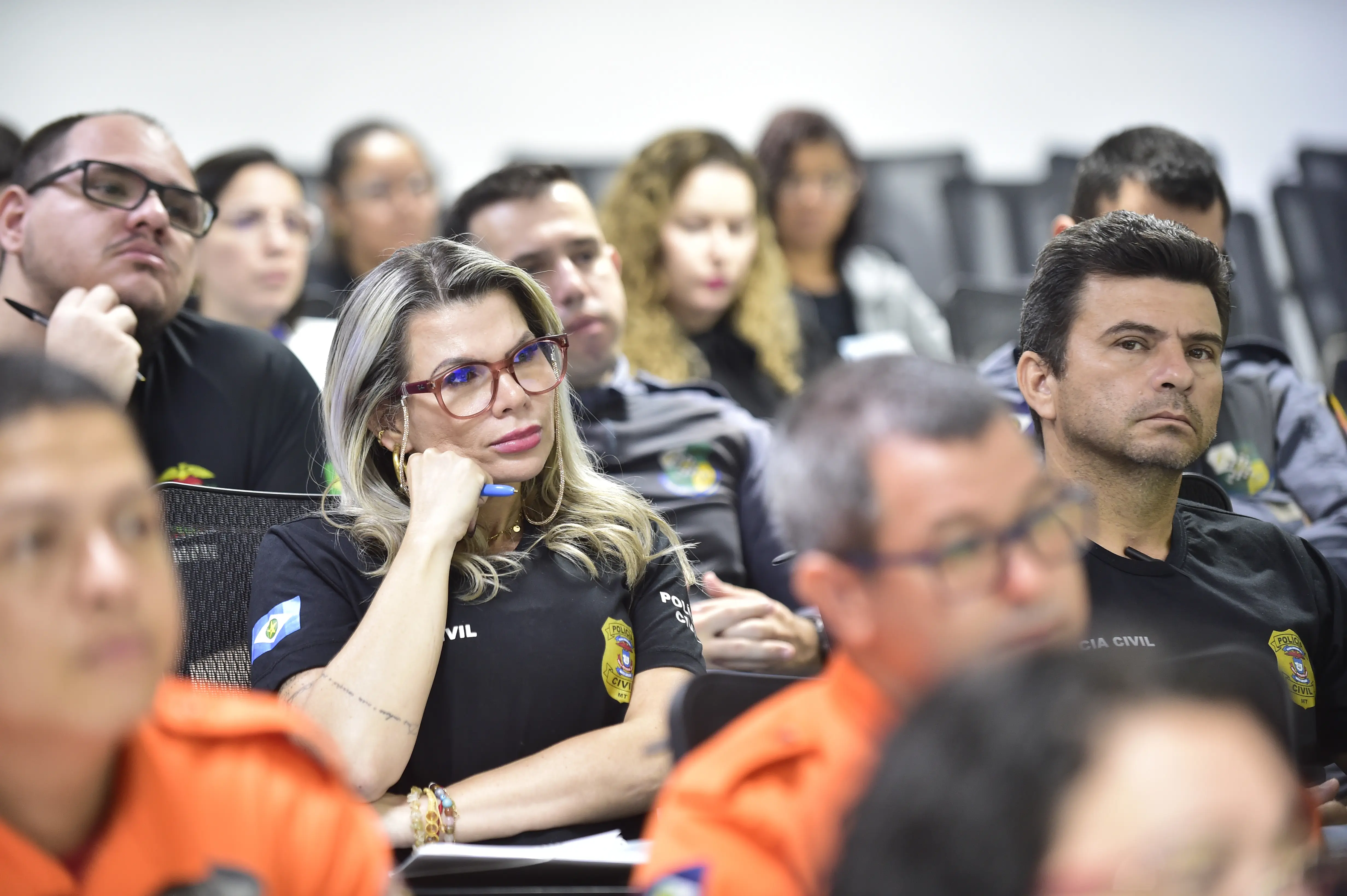Foto que mostra profissionais da Segurança Pública uniformizados, sentados em carteiras na sala de aula da Escola dos Servidores do Poder Judiciário. É possível identificar policiais civis e militares, bombeiros militares. Em primeiro plano, aparece uma policial civil prestando atenção na aula.
