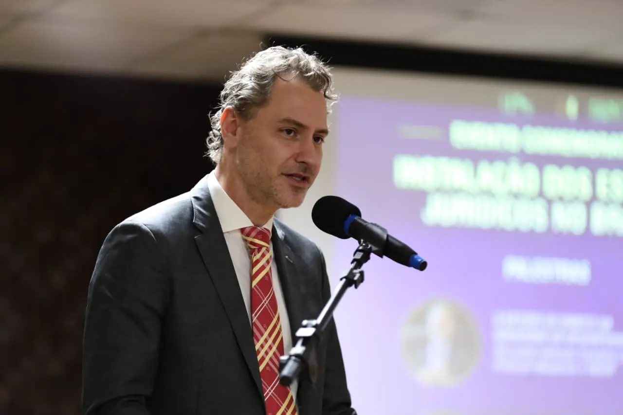 Henrique Garbellini Carnio é um homem branco e usa terno cinza escuro, camiza branca e gravata vermelha
