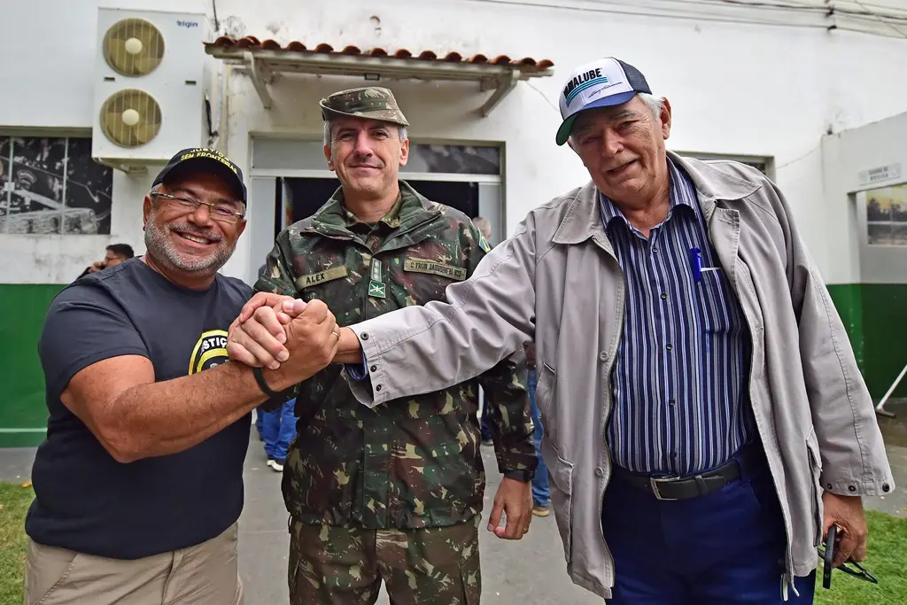 Juiz José Antônio Bezerra Filho, o coronel Alex, do Exército; e o secretário de Assuntos Estratégicos de Cáceres posam para a foto, sorrindo, Eles estão com as mãos unidas.