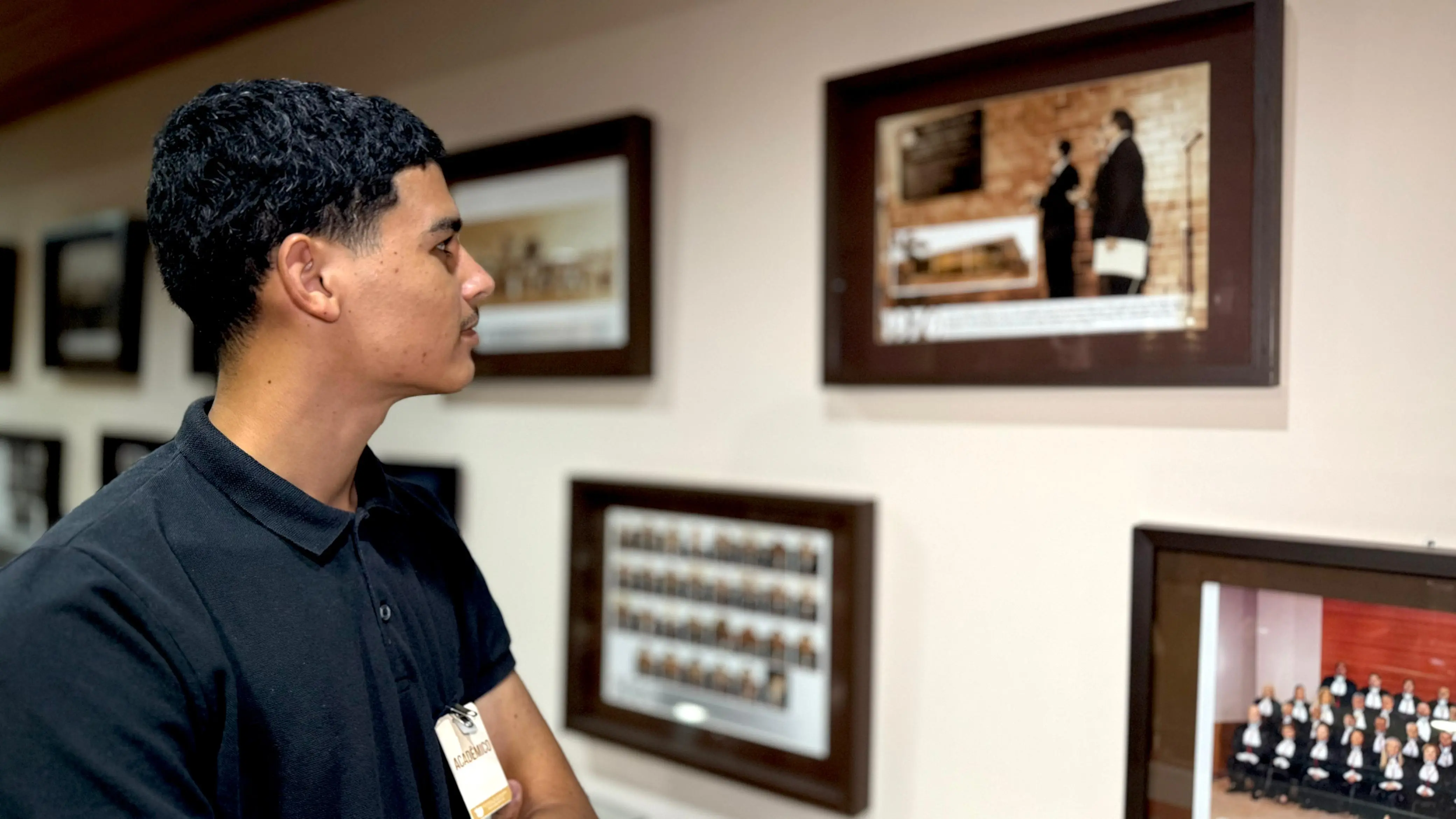 Rapaz, Estudante de Direito, observa quadros de fotos expostos na parede do Espaço Memória do Tribunal de Justiça.
