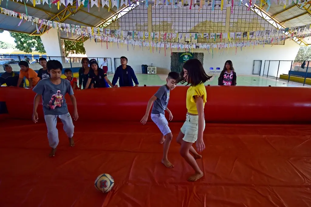 Crianças brincam em um campo de futebol inflável, numa quadra esportiva.