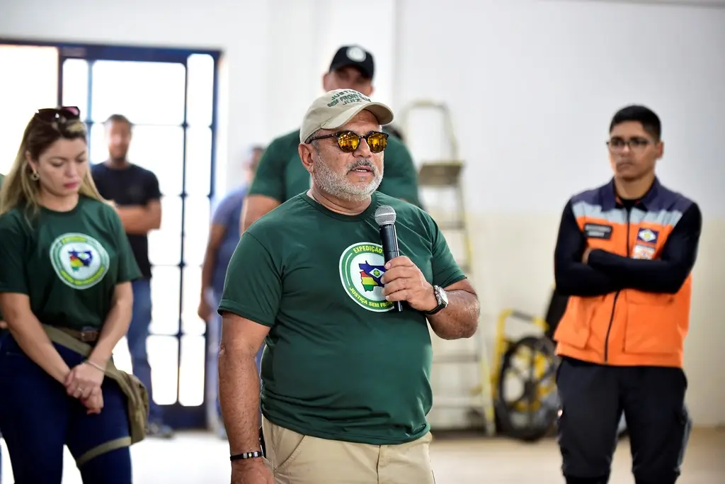 Juiz José Antônio Bezerra Filho em pé, falando ao microfone, no pátio de uma escola. Ele está usando camiseta verde da Justiça Sem Fronteiras e há pessoas em volta dele, ao fundo da foto.